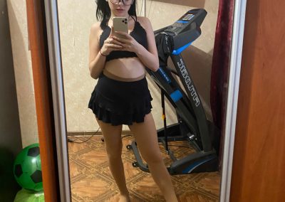 Girl in skirt and bra and pantyhose taking selfie in mirror