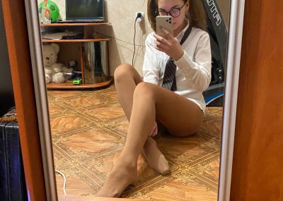 Woman with pigtails and glasses and schoolgirl shirt on sitting in floor in pantyhose taking selfie