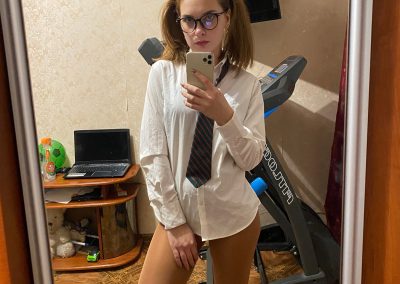 Girl with pigtails and glasses in schoolgirl shirt taking selfie in her pantyhose