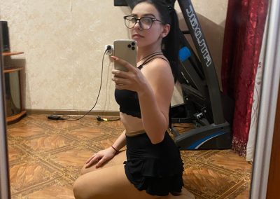 Sexy girl wearing glasses in sports bra and skirt and pantyhose on her knees taking selfie