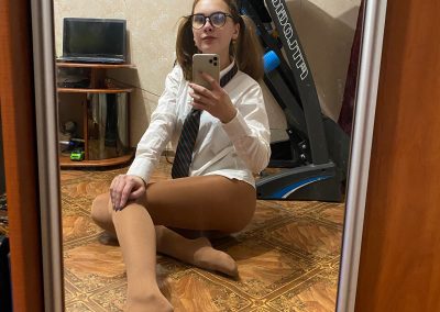 Girl with pigtails and glasses in schoolgirl shirt and tan pantyhose taking selfie