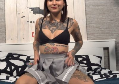 Tattooed woman in miniskirt,sports bra and pantyhose kneeling on bed