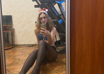 Pretty girl in pantyhose and santa hat sitting on ground taking selfie