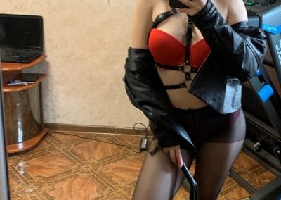 Pretty amateur woman in leather hat and coat with whip taking sexy selfie in black pantyhose