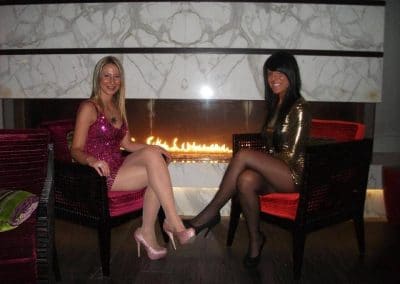 Blonde In Nude Pantyhose and Brunette in Black Pantyhose Sitting With Legs Crossed